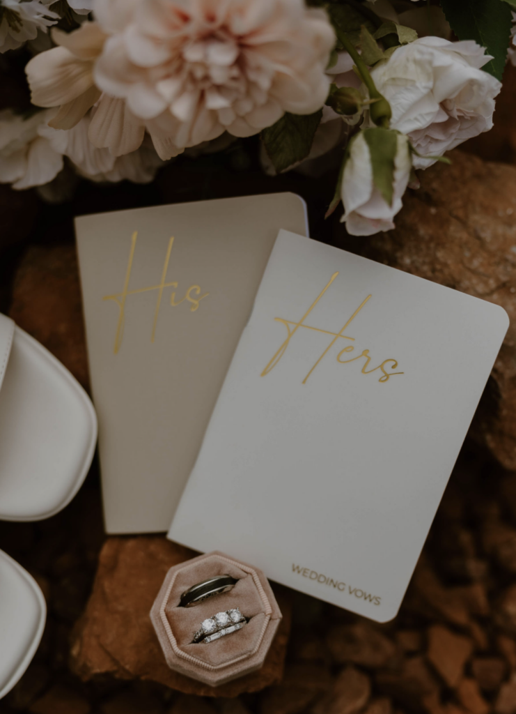 Custom flat lay with wedding day florals with wedding rings and his and hers vow books